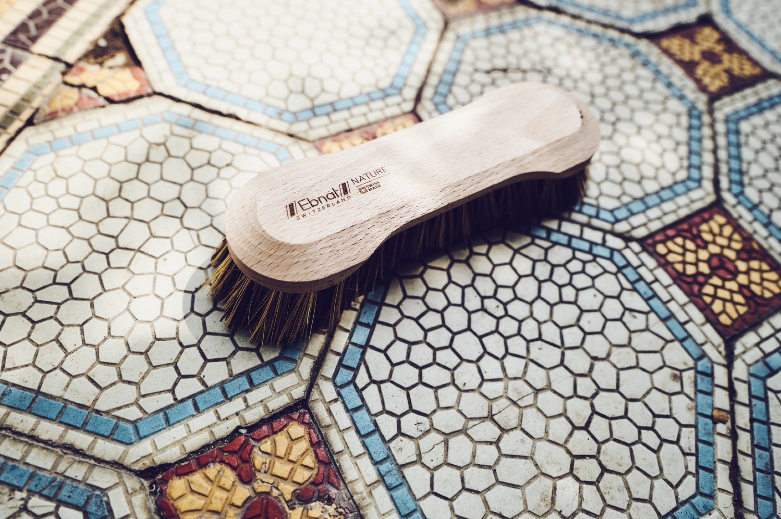 nachhaltige Handbürste aus Holz der Ebnat AG – aufgenommen auf kunstvoll gemustertem Mosaikboden mit blauen und roten Details.