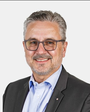 Ein Verkaufsmitarbeiter der Firma Ebnat AG im mittleren Alter l&auml;chelt. Er tr&auml;gt eine graue Brille und hat ein blaues Hemd mit einem schwarze Blazer an. Seine Haare sind grau/weiss. Er hat einen kurzen und weissen Bart.