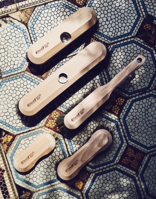 Verschiedene Holzbürsten aus der NATURE-Linie der Ebnat AG liegen auf einem kunstvoll gemusterten Mosaikboden – natürliche Materialien treffen auf traditionelles Design.