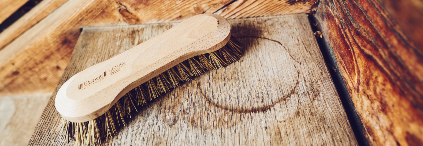 Handbürste aus Holz mit Naturborsten der Ebnat AG – fotografiert auf einer rustikalen Holzoberfläche in natürlicher Umgebung.