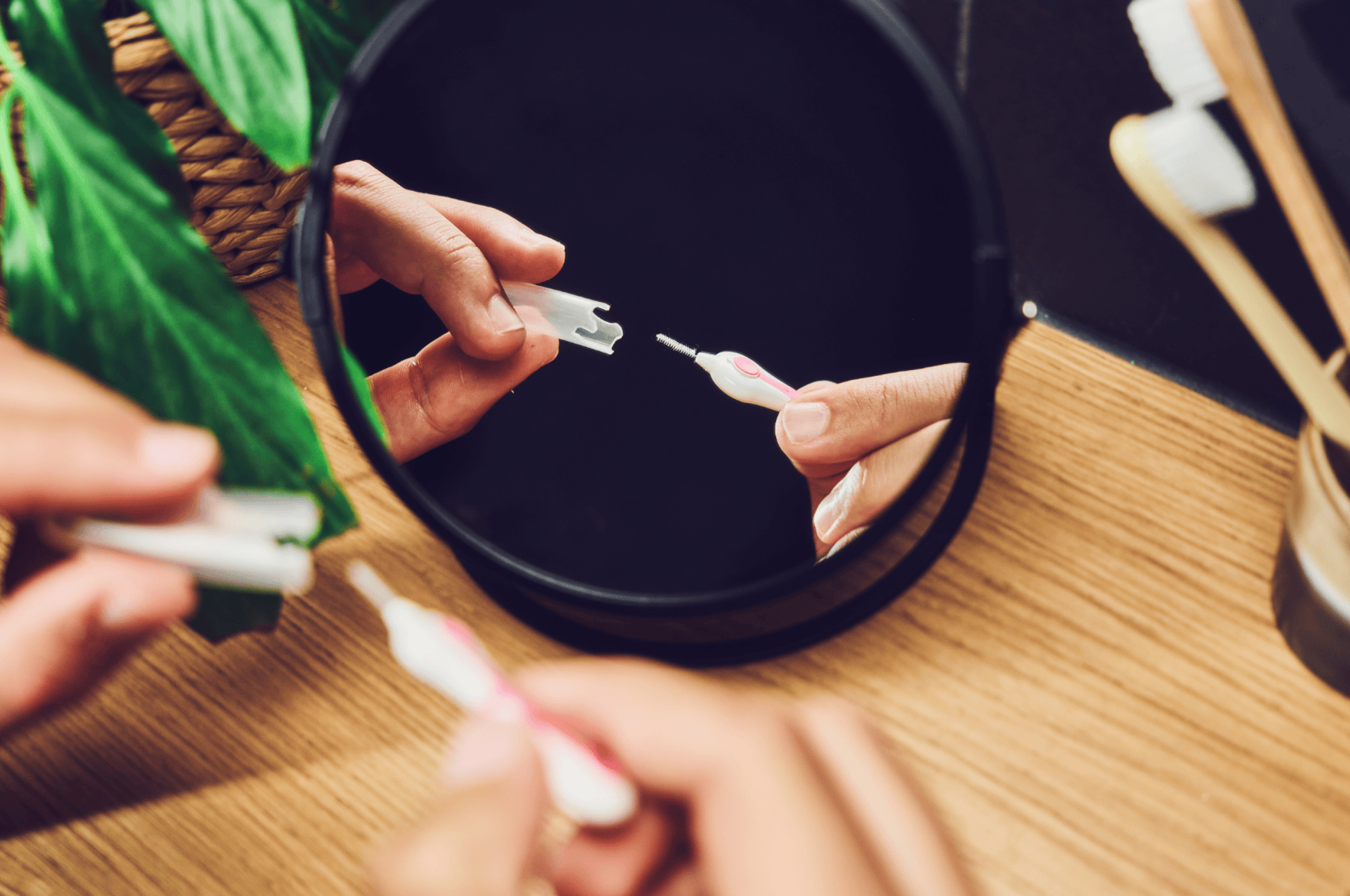 Nahaufnahme eines Badezimmers mit Fokus auf der Hand einer Person, die eine Interdentalbürste der Ebnat AG vor einem Spiegel benutzt – im Hintergrund Pflanzen, Zahnbürsten und natürliche Materialien.
